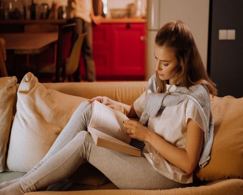A person reading a book on a sofa with warm evening light